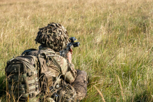 camouflaged soldier in grass carrying MOLLE pack