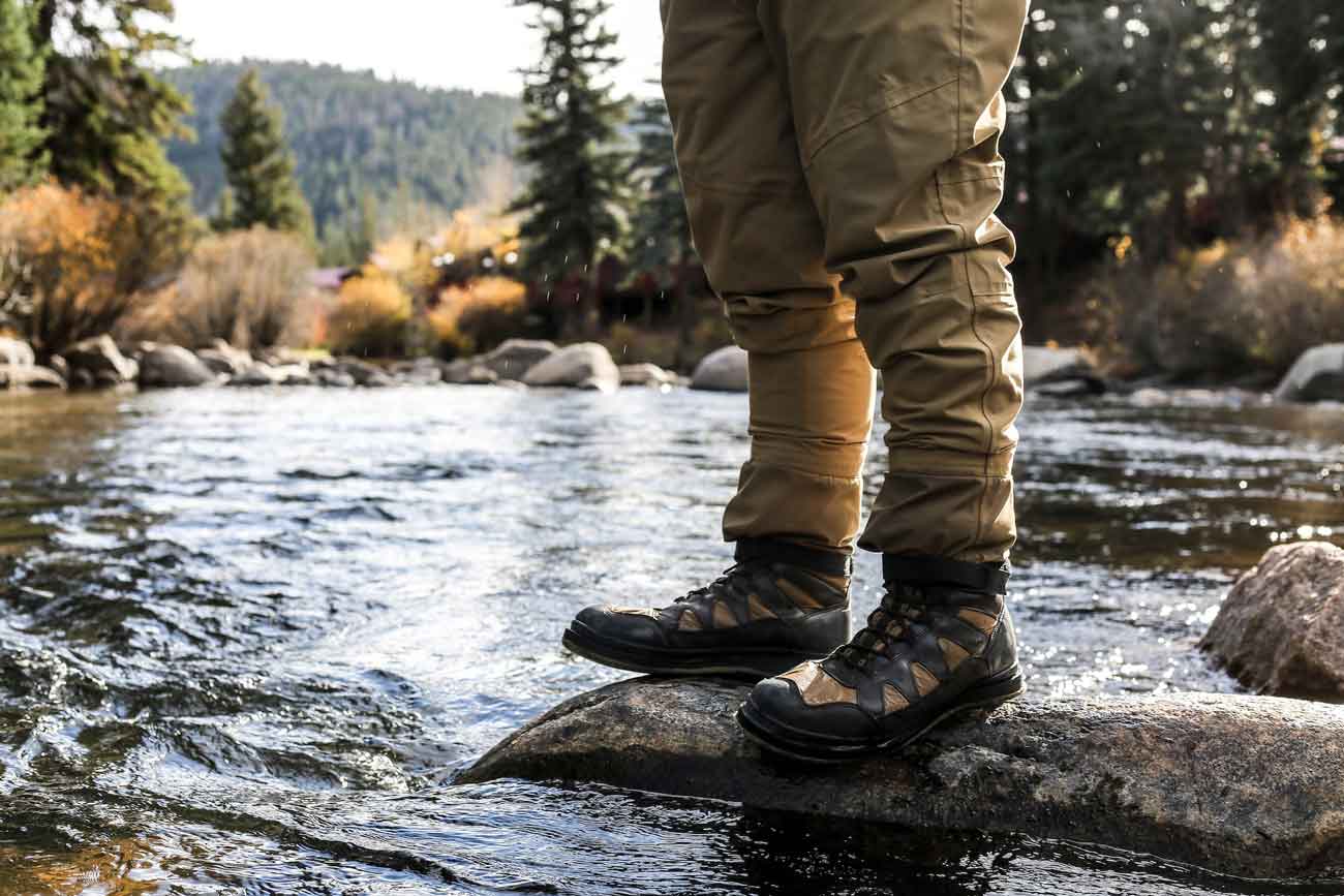 person in tactical shoes standing on stone in a river